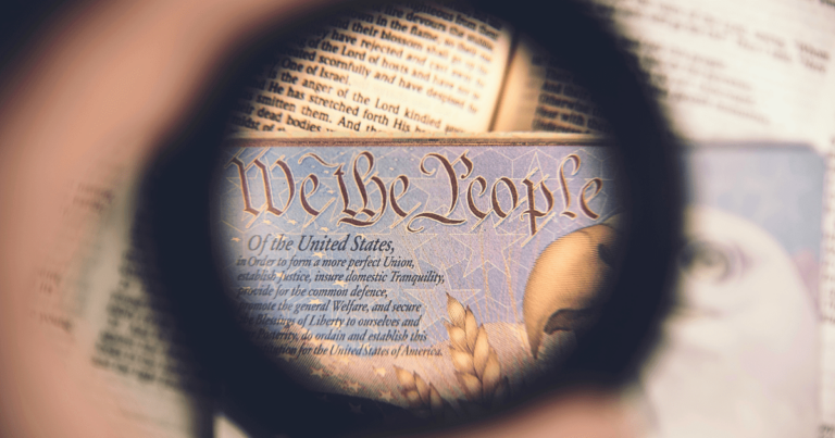 Looking through the lens of a magnifying glass at the Declaration of Independence, focused on the words "We the People"